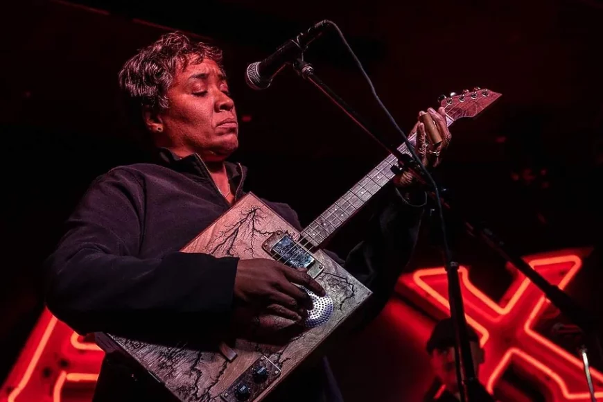 Female blues musician onstage playing cigar box guitar.